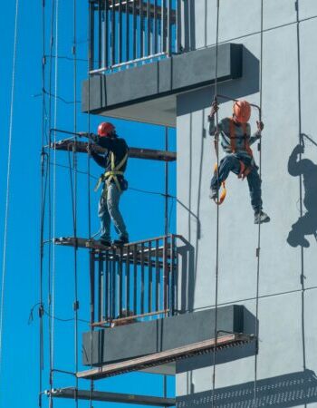 Couple of workers fixing and climbing a scaffolding while following all the safety measures